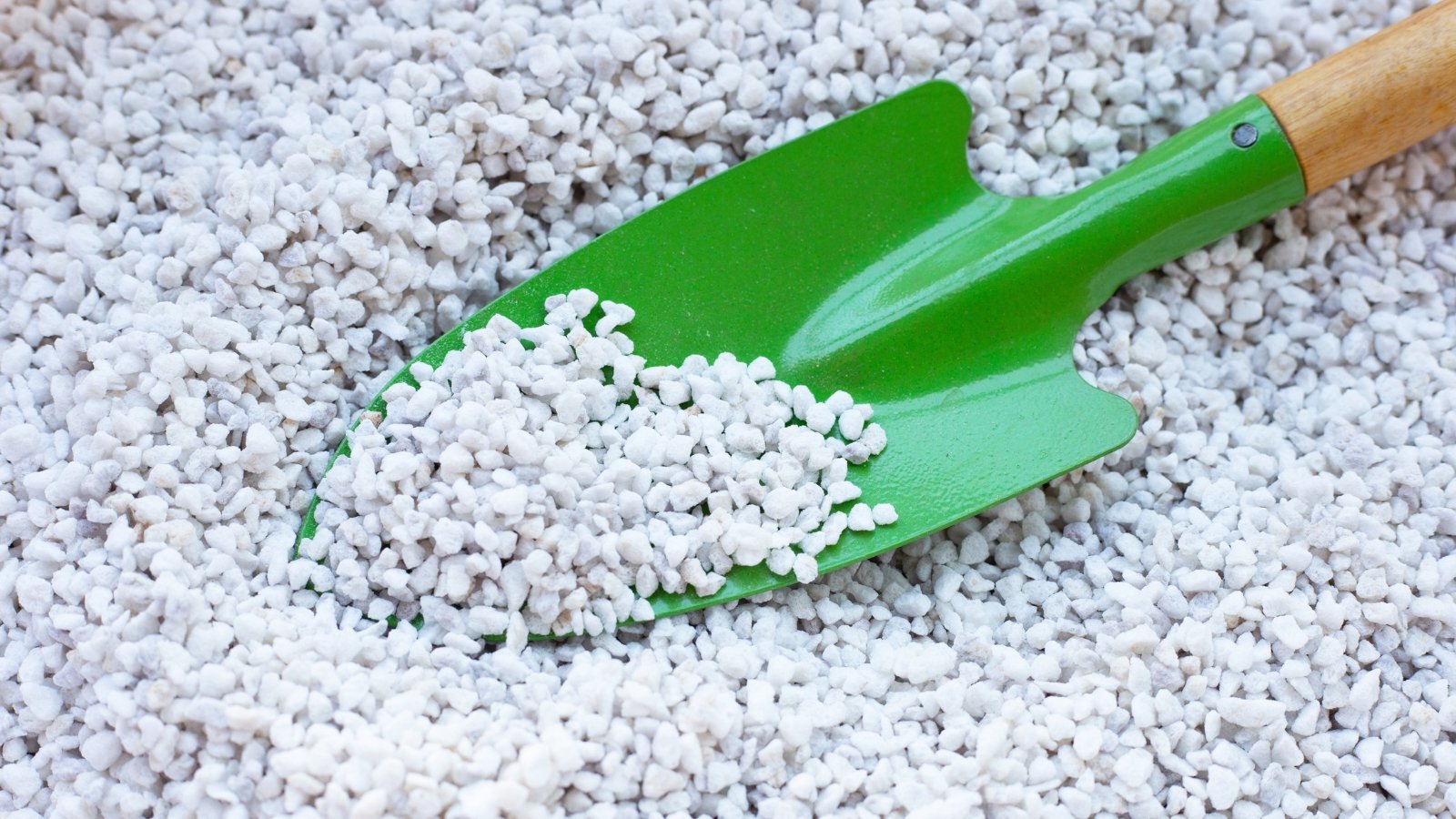 Close up of a bright green shovel scooping a pile of small, white pebbles.